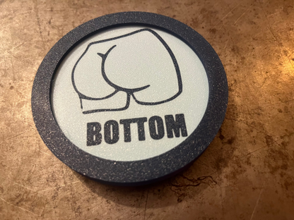Round coaster with a butt graphic and 'BOTTOM' text on a brown surface