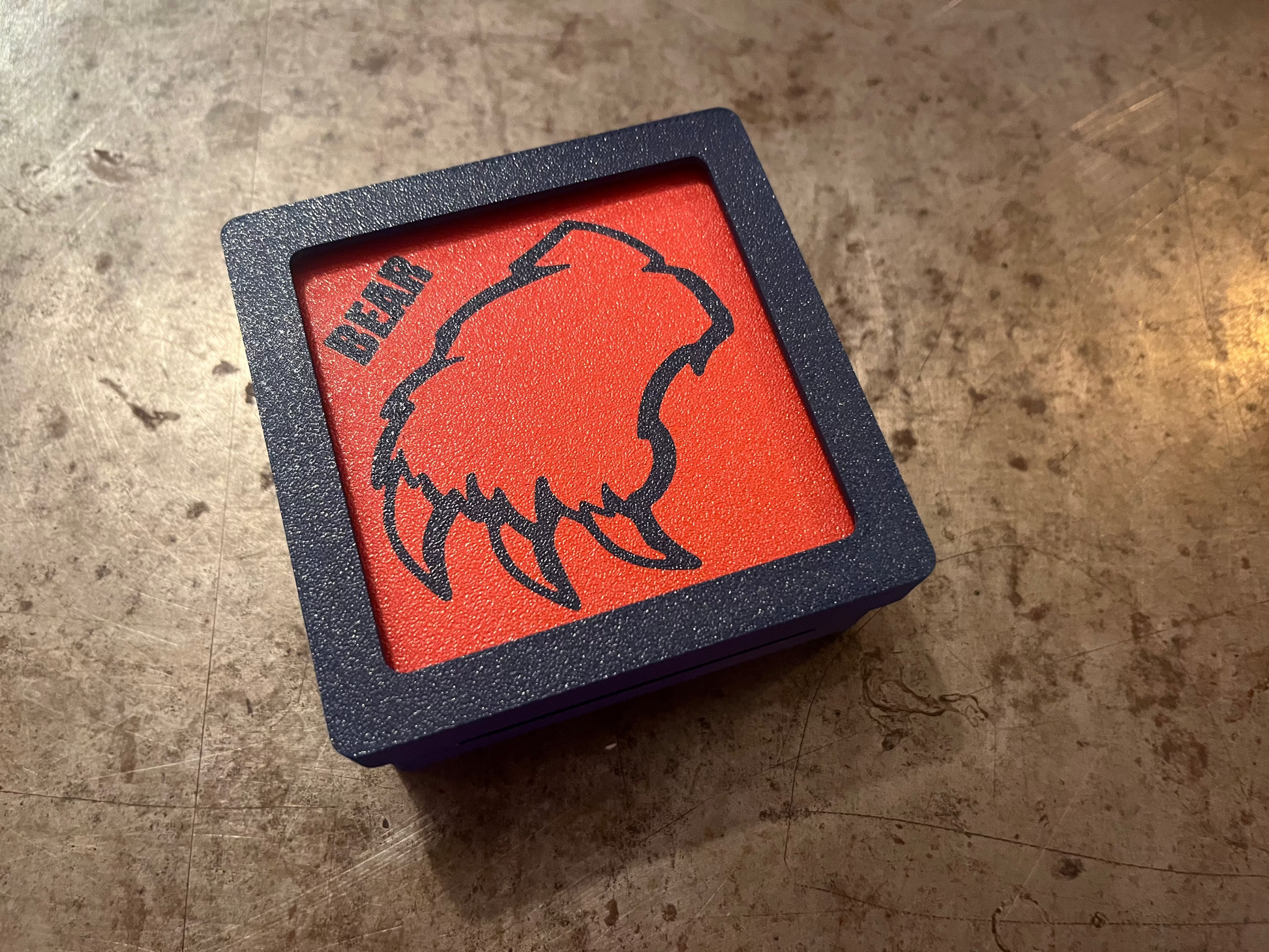 Red square with bear design and 'BEAR' text on a textured surface