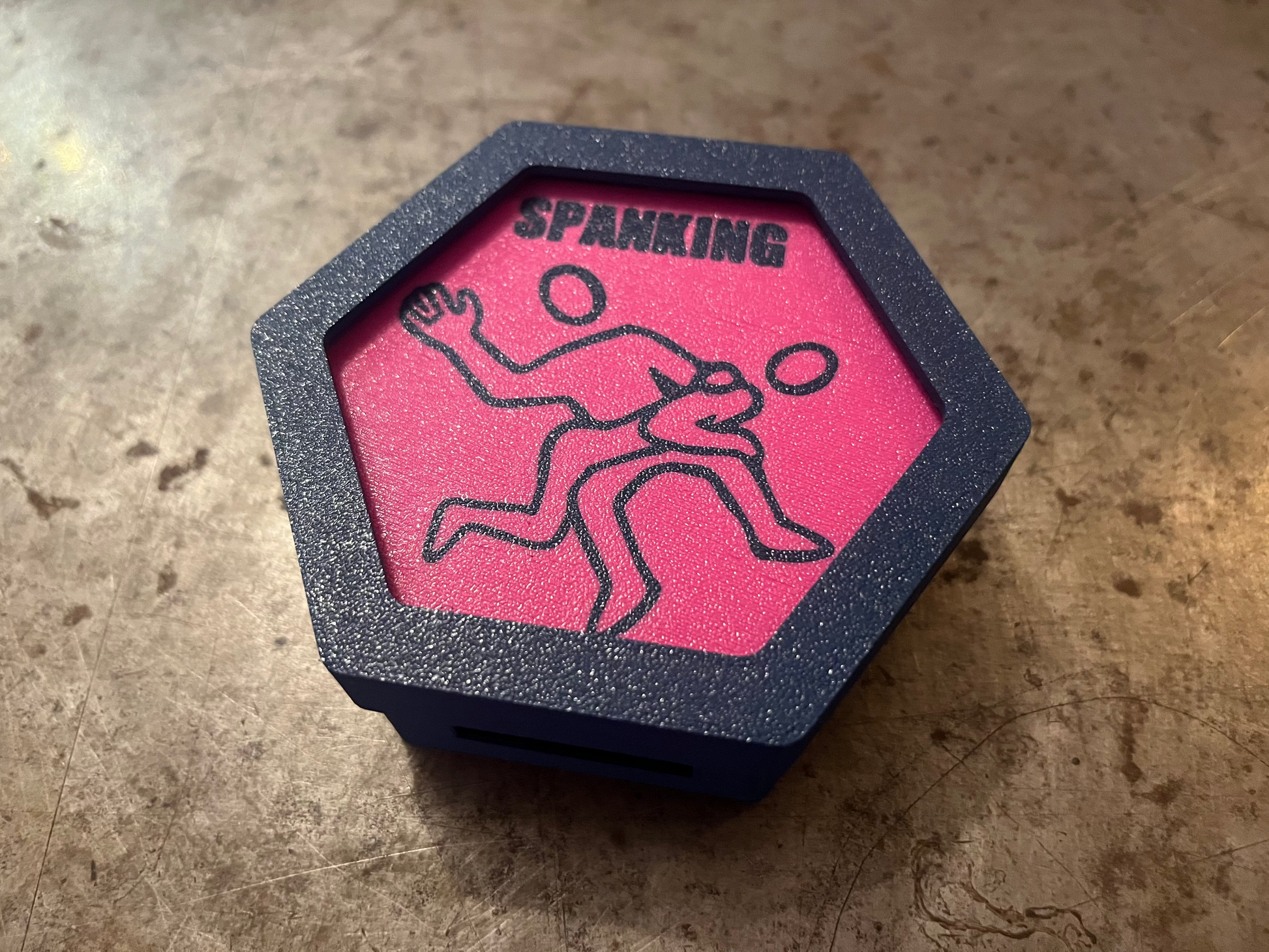 Hexagonal object with pink center and black design on a textured surface